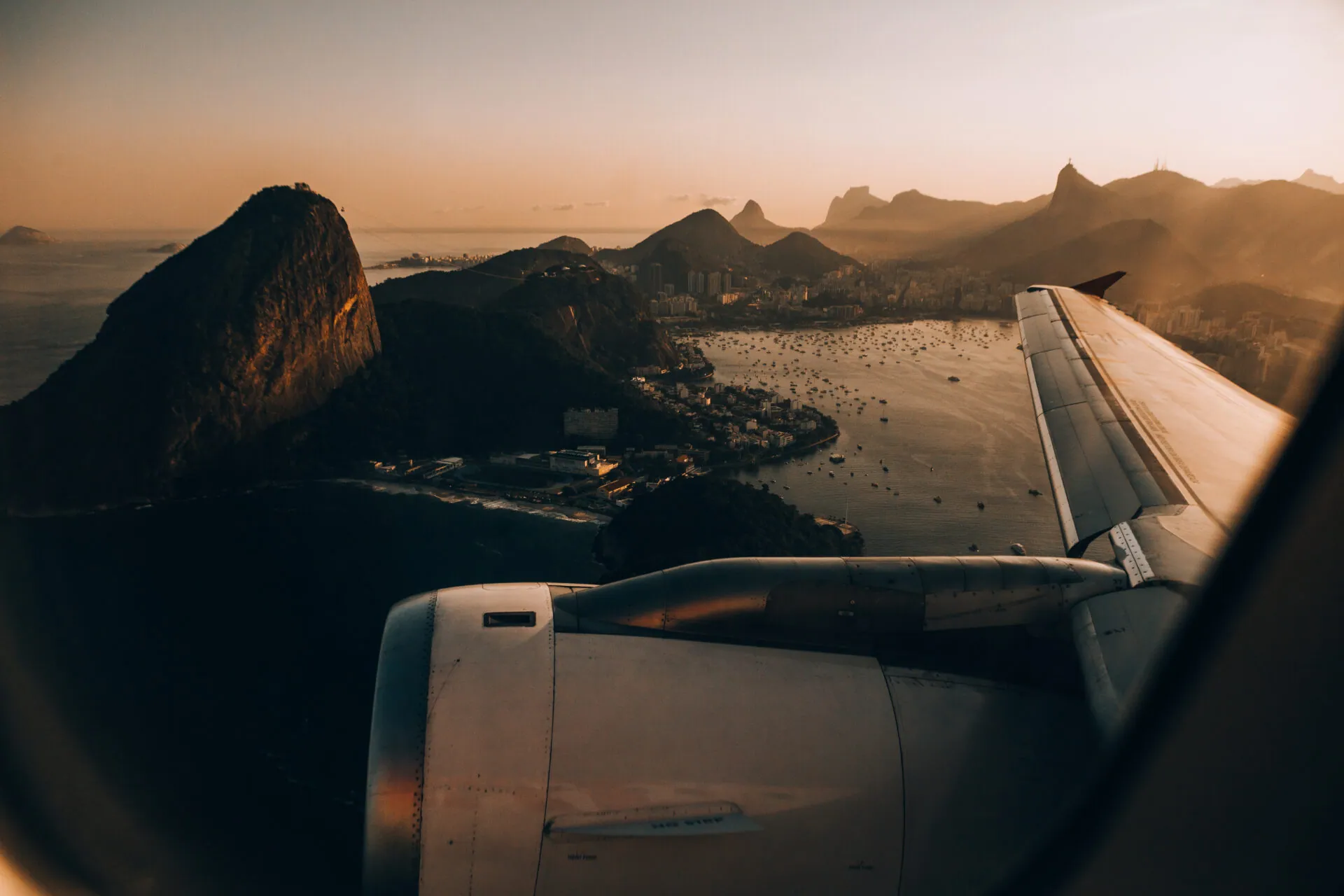 Aircraft wing and engine above a mountainous coastal bay at sunset