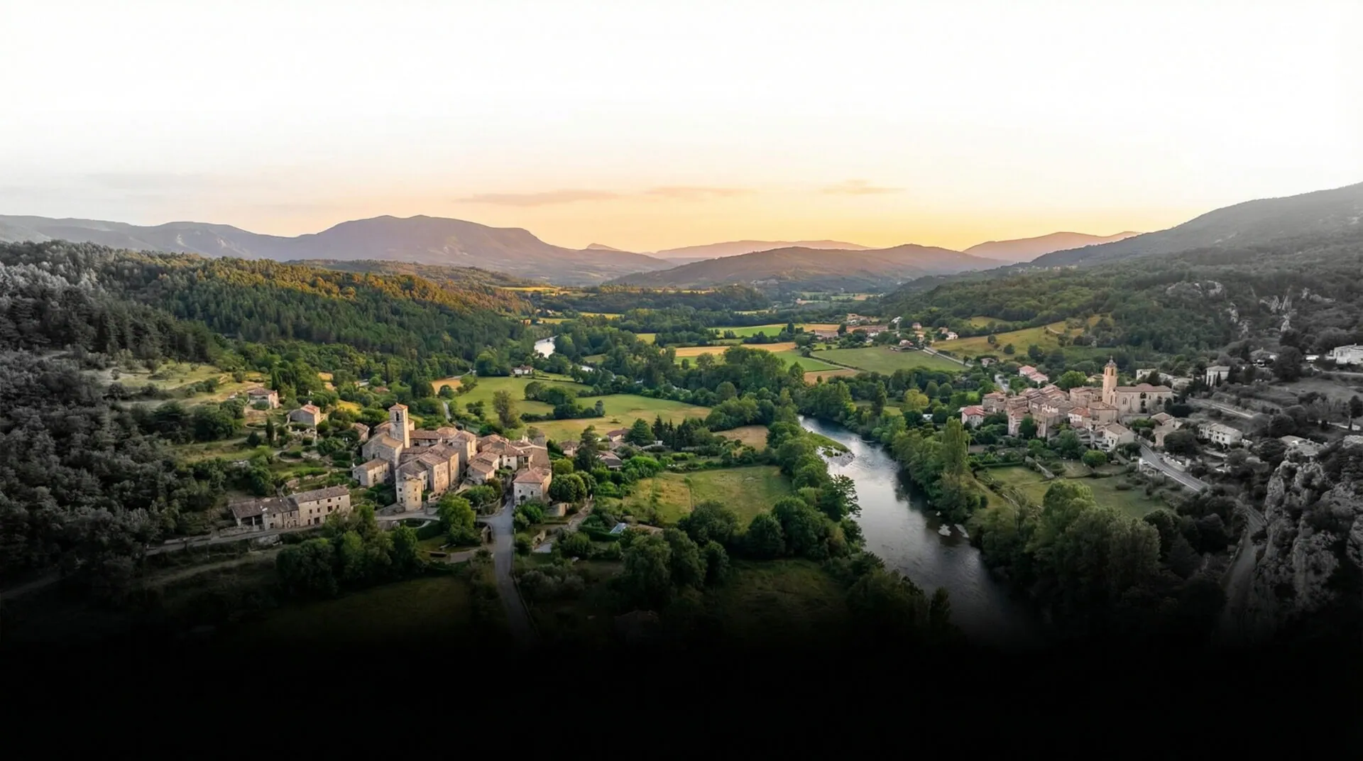 Aerial view of a green river valley and hilltop village at dusk