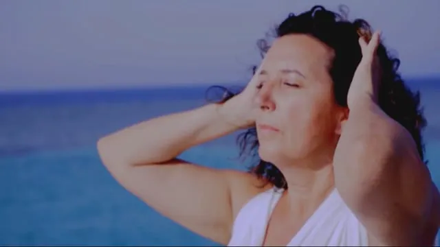 Woman with eyes closed and hands in her hair beside a calm blue sea