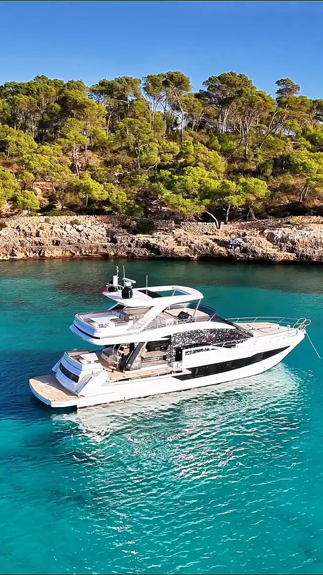 White motor yacht anchored in a turquoise cove lined with pine trees