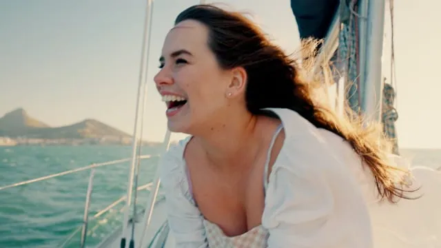 Woman laughing with windswept hair aboard a sailboat on open water