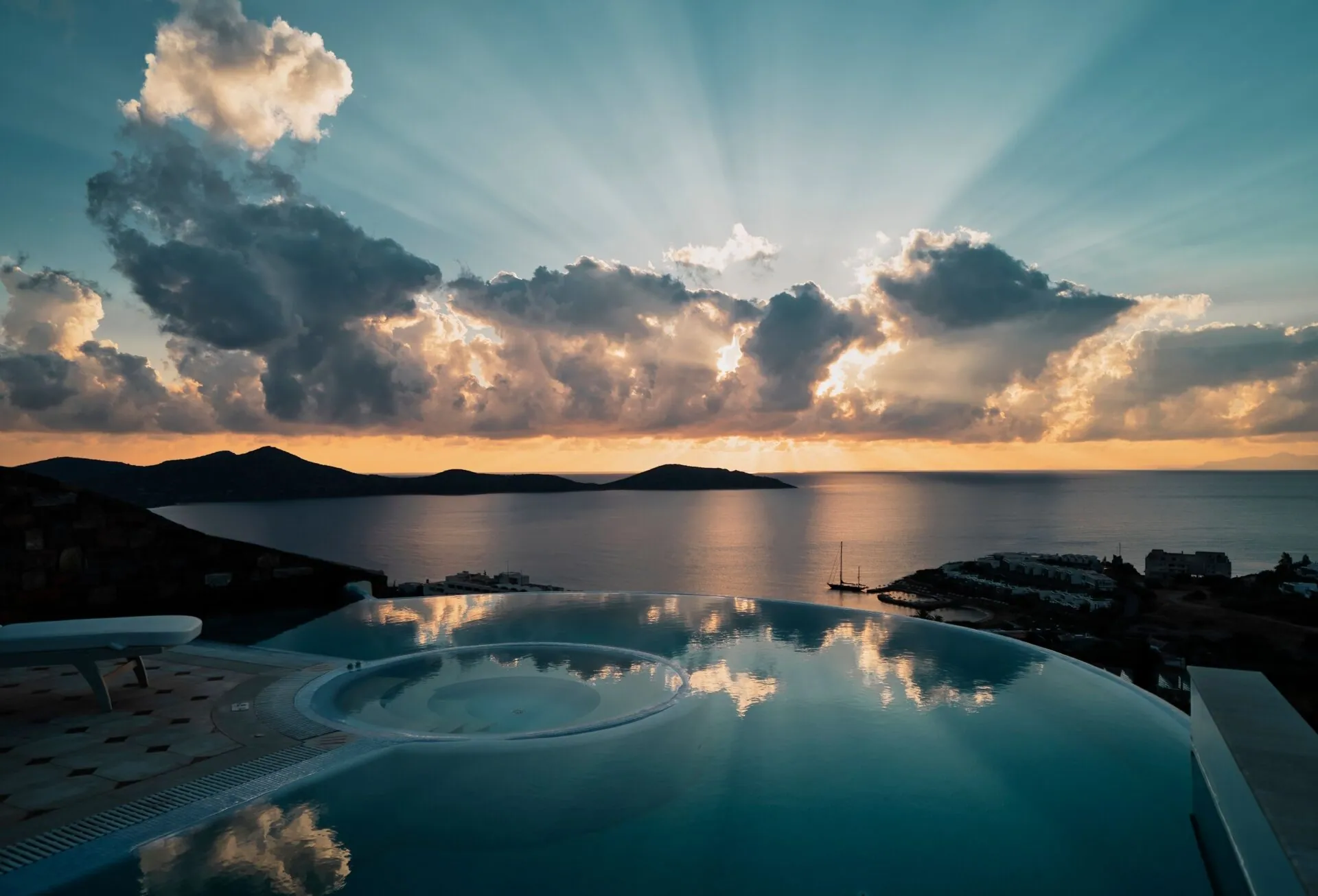 Infinity pool reflecting dramatic clouds and sun rays over a quiet bay
