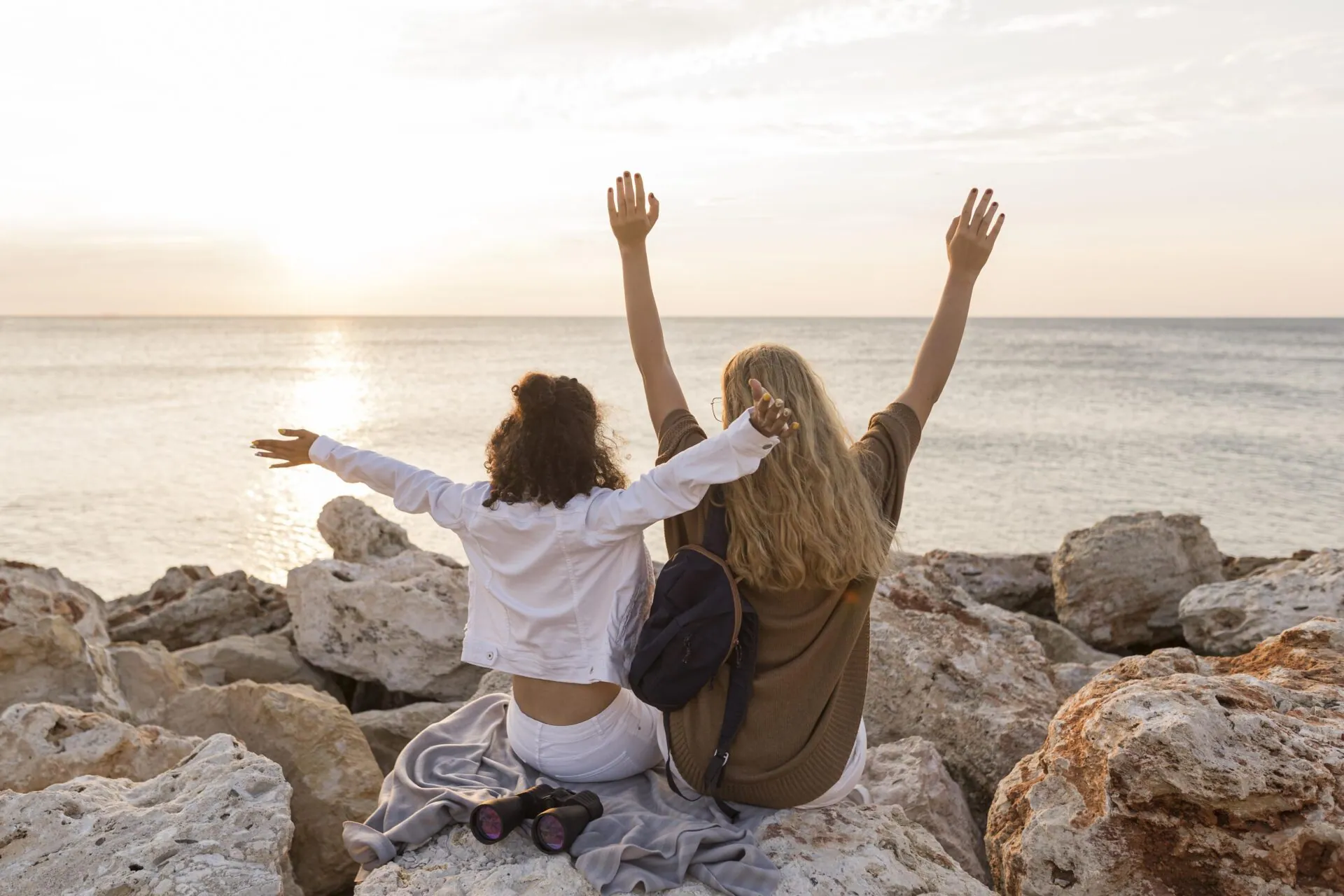 Two friends raising their arms on seaside rocks at sunrise