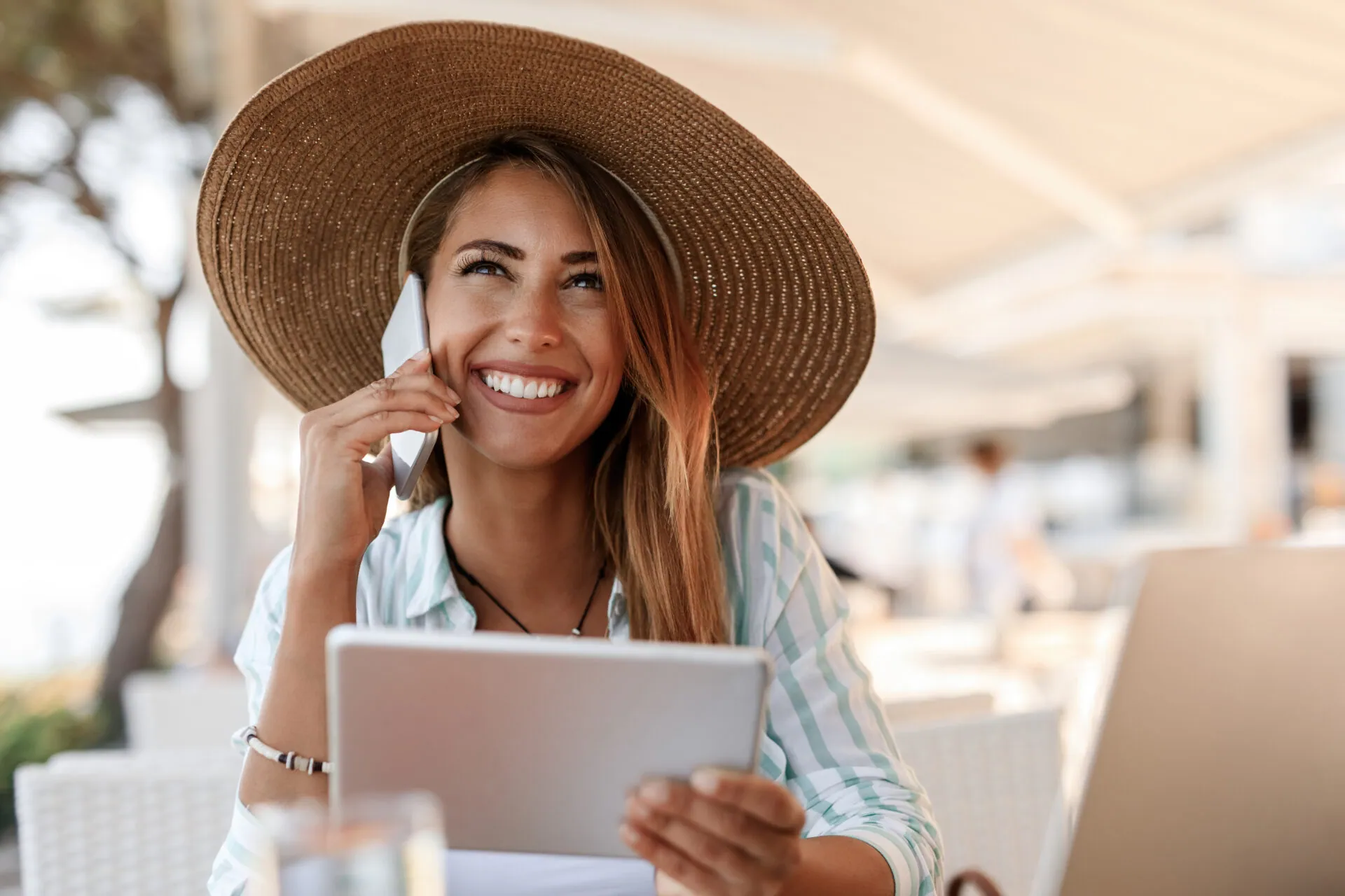 Smiling woman in a wide straw hat on the phone at a seaside cafe