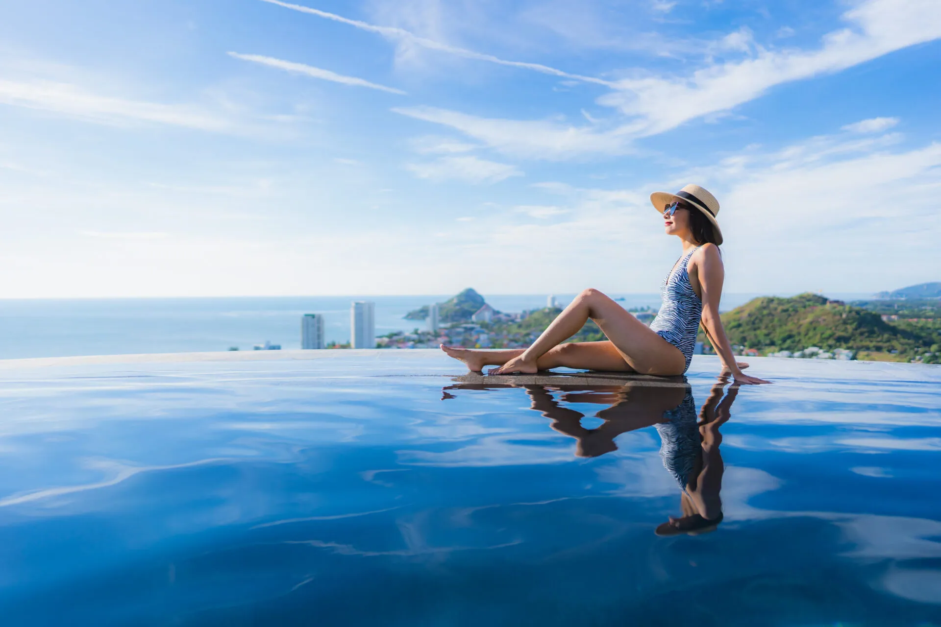 Woman in a sun hat relaxing at the edge of a rooftop infinity pool