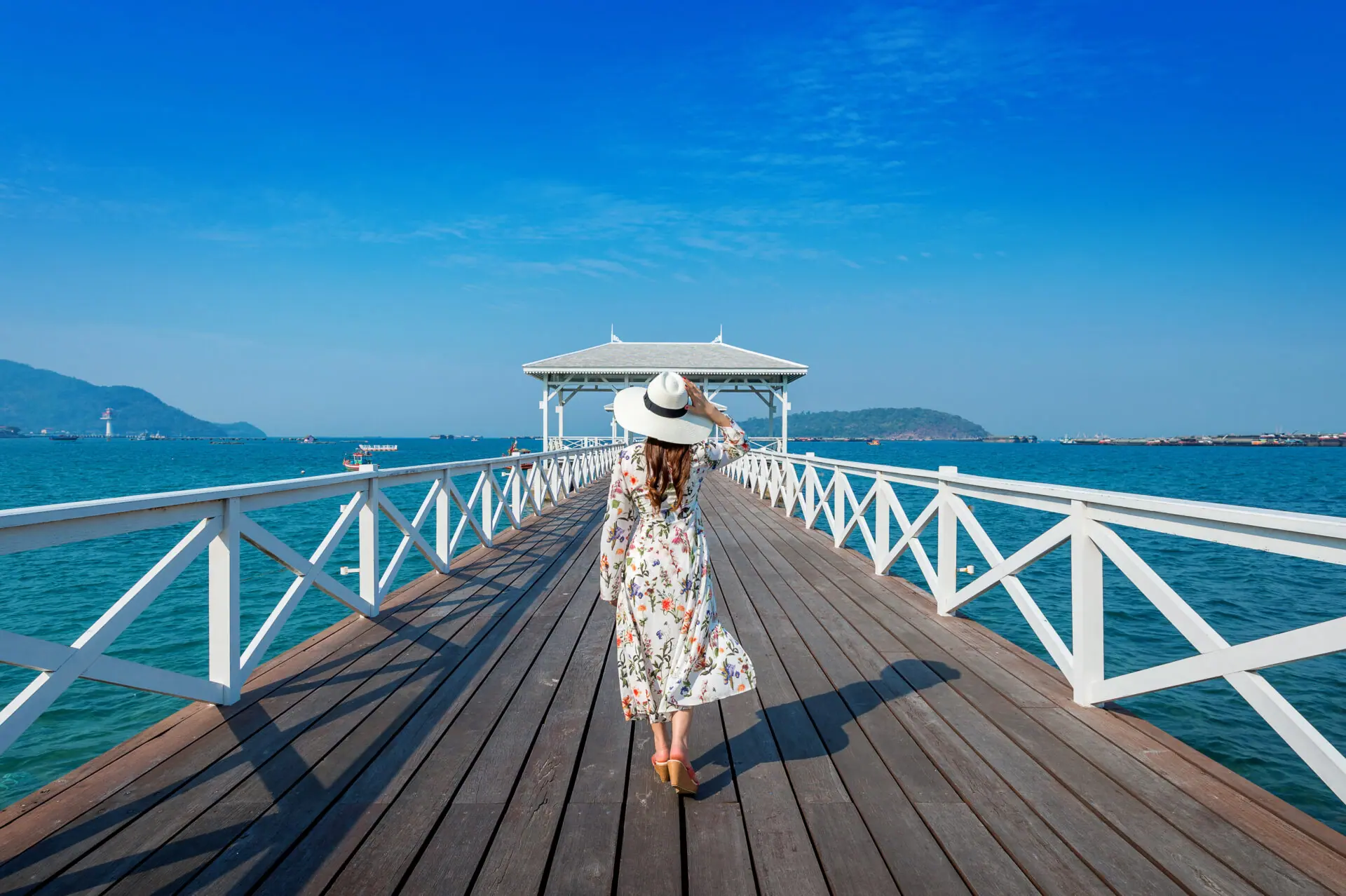 Woman in a floral dress walking a white pier toward a seaside gazebo
